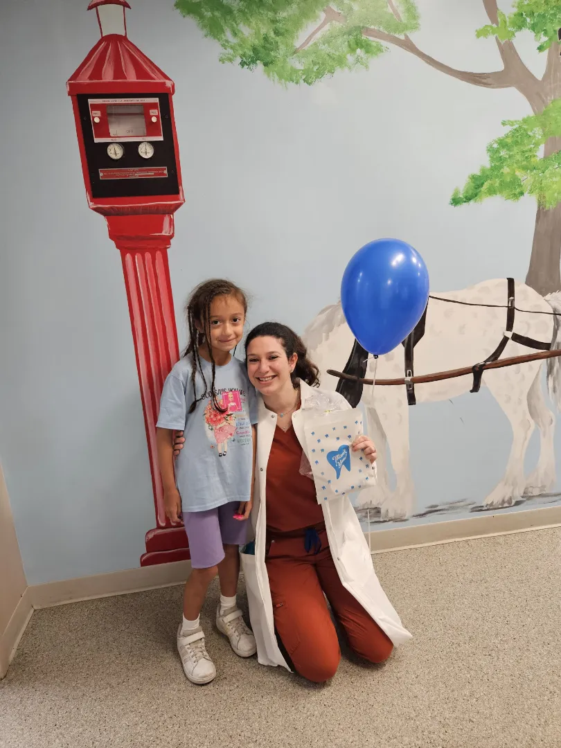 A Dental Care Kids patient with a team member by the hand-painted mural