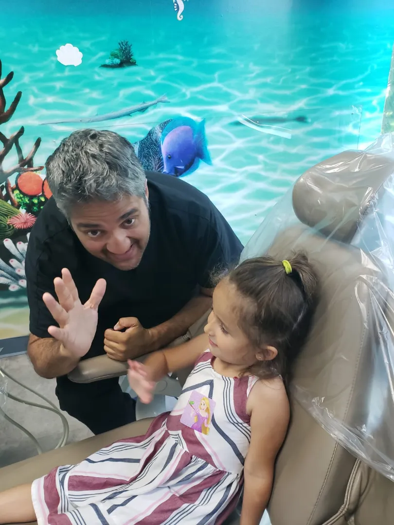 A Dental Care Kids team member waving beside a young patient during an adaptive visit
