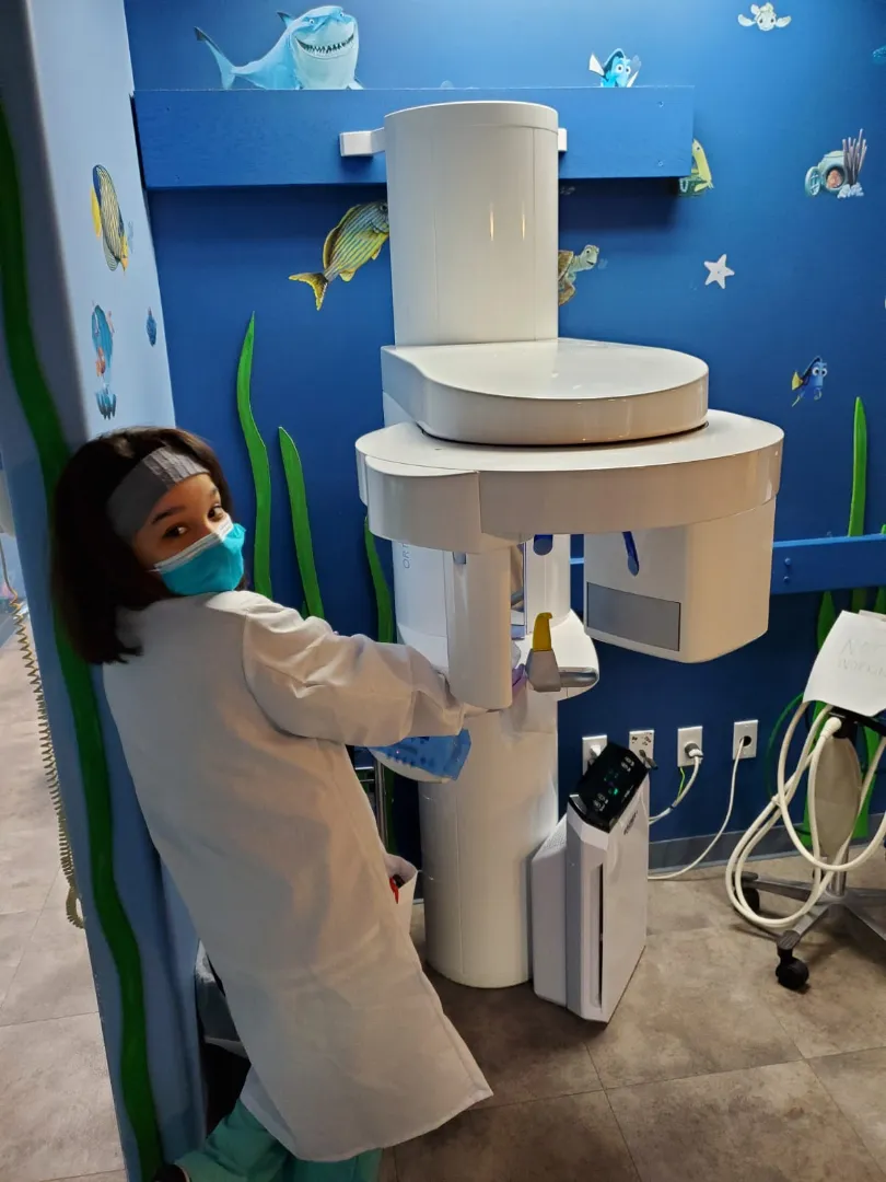 A young Dental Care Kids patient beside the panoramic digital X-ray machine in the underwater-mural room