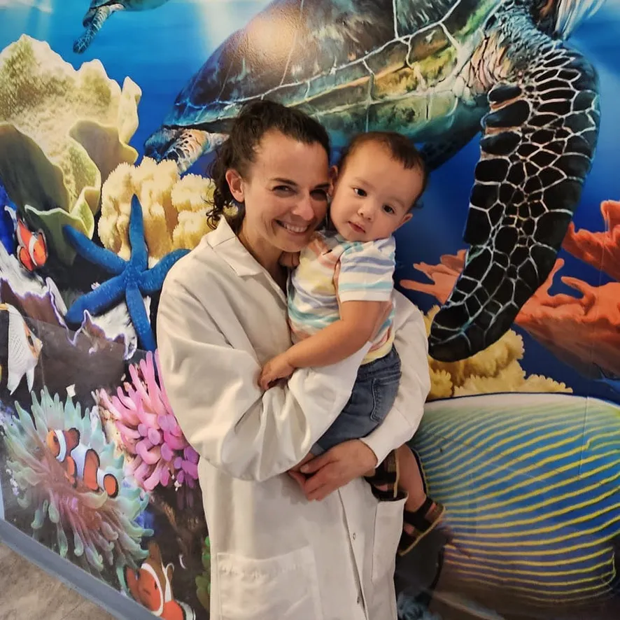 A Dental Care Kids team member holding a toddler by the turtle mural