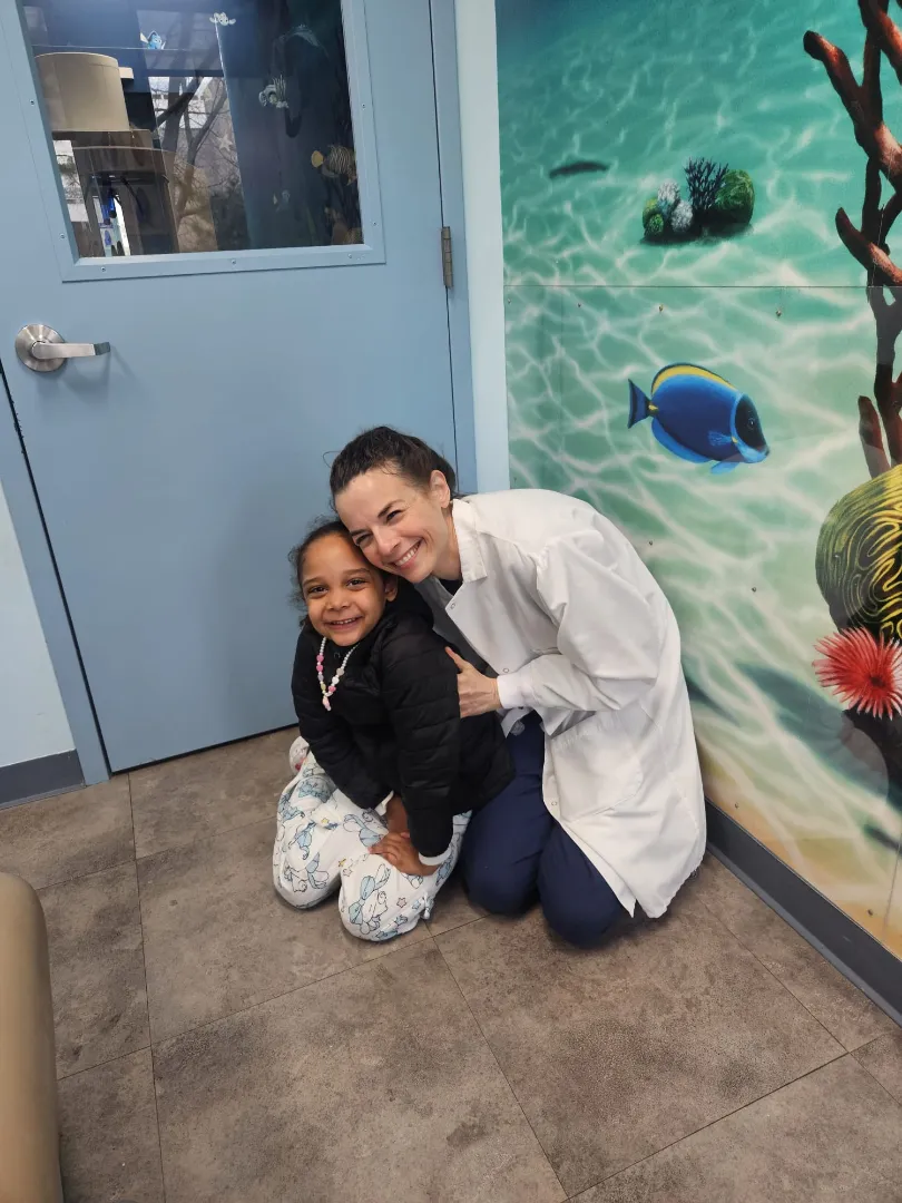 Dental Care Kids patients hugging a team member by the fish mural