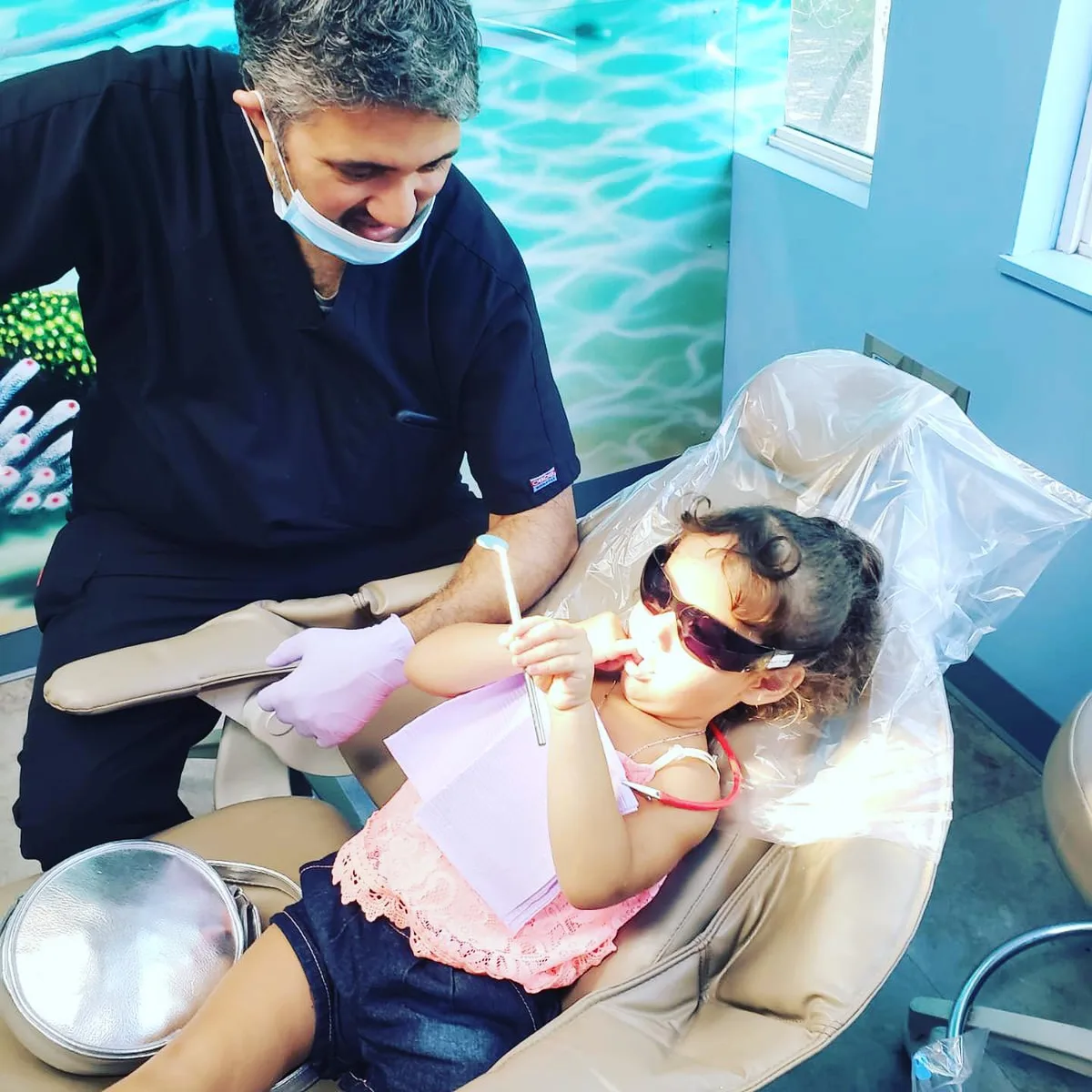 A Dental Care Kids dentist working gently with a young patient wearing protective sunglasses